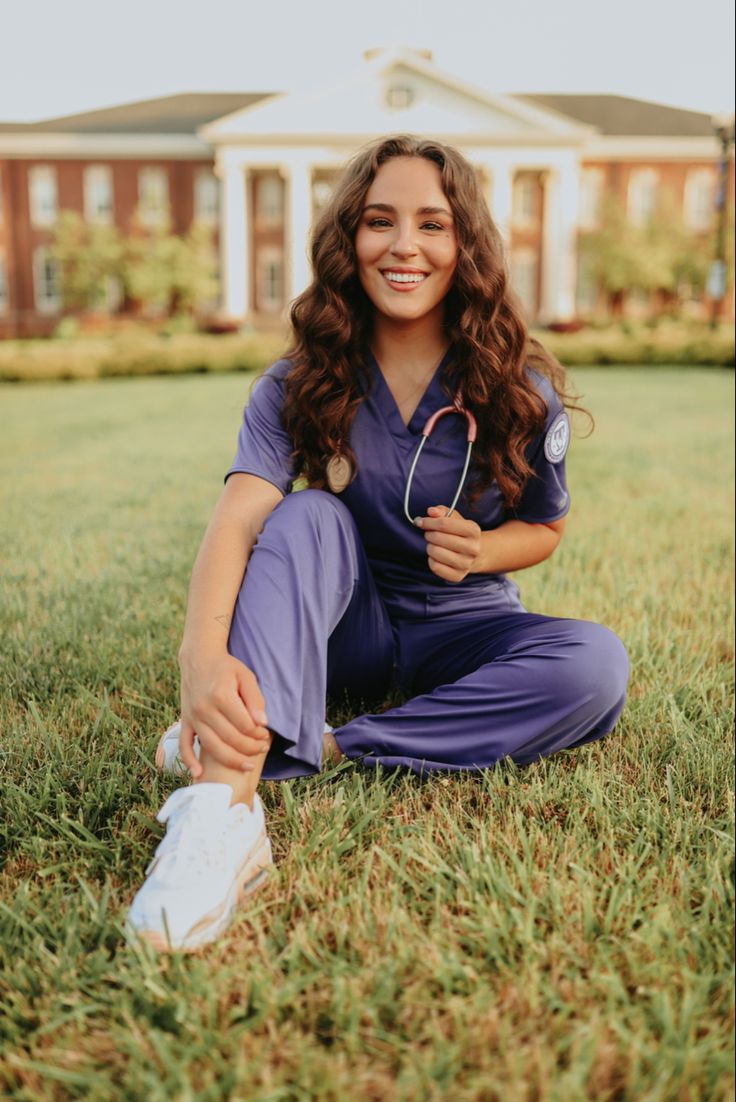 a woman in scrubs sitting on the grass with a stethoscope around her neck