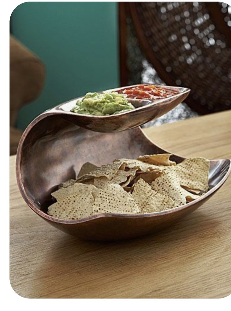 a bowl filled with chips and guacamole on top of a wooden table