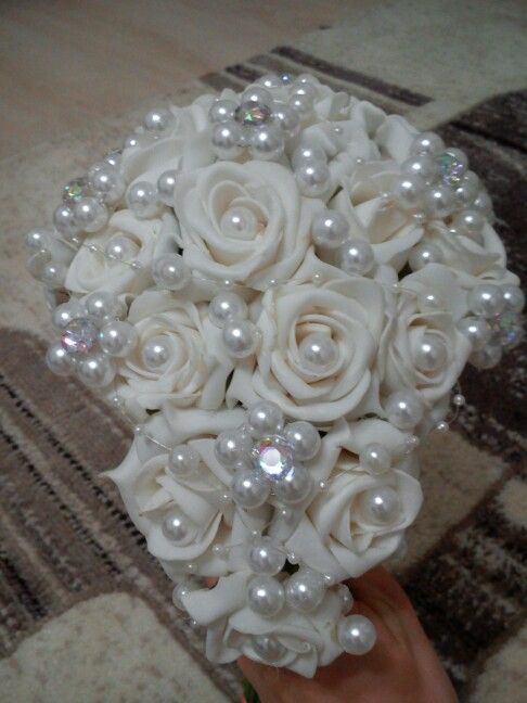 a bridal bouquet with white roses and pearls is held by someone's hand