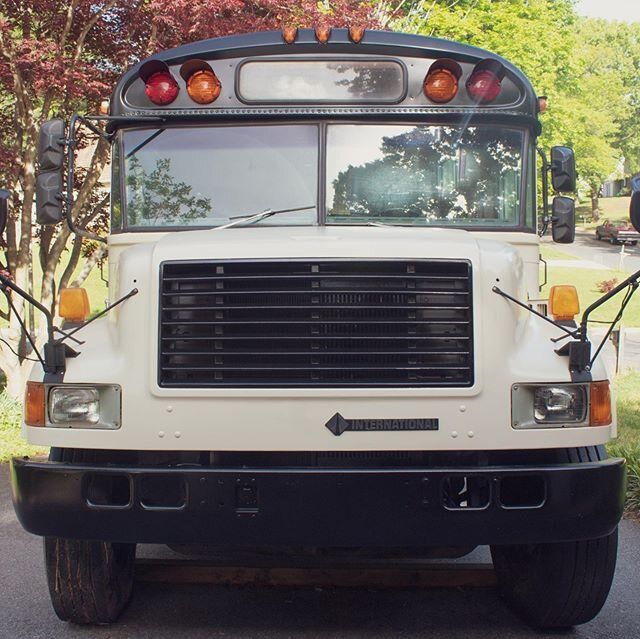 the front end of a white school bus parked in a parking lot next to trees