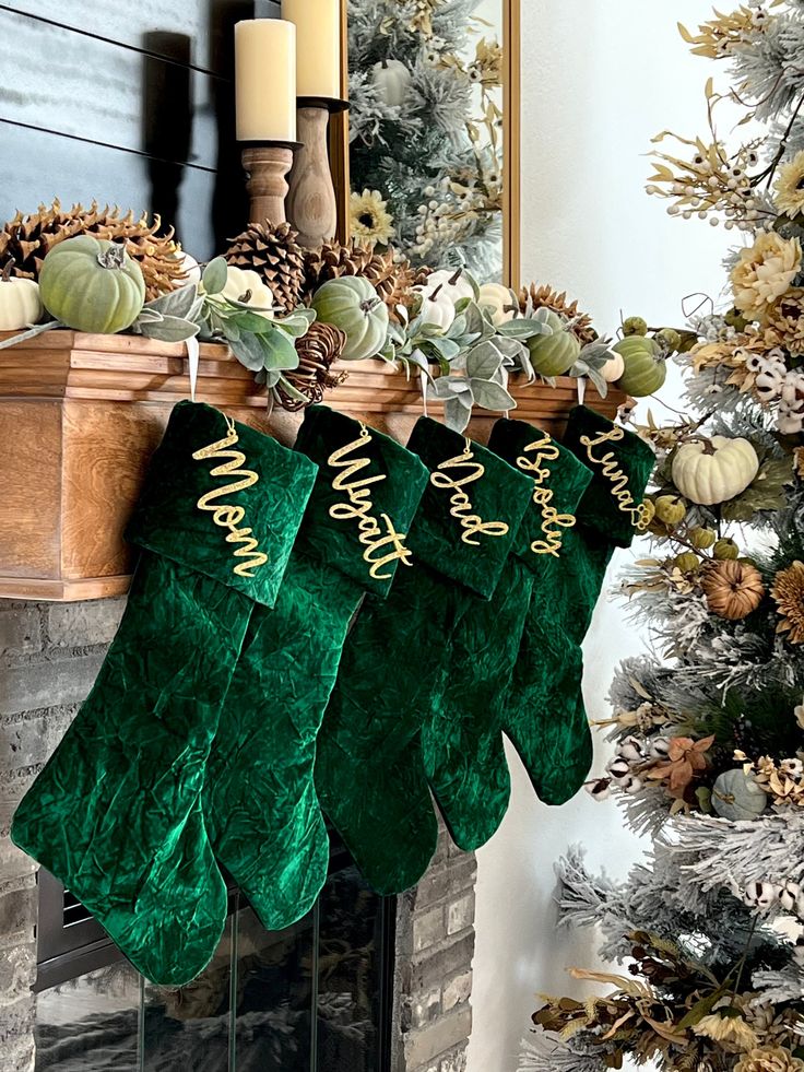 christmas stockings hanging from a mantel decorated with pine cones and greenery