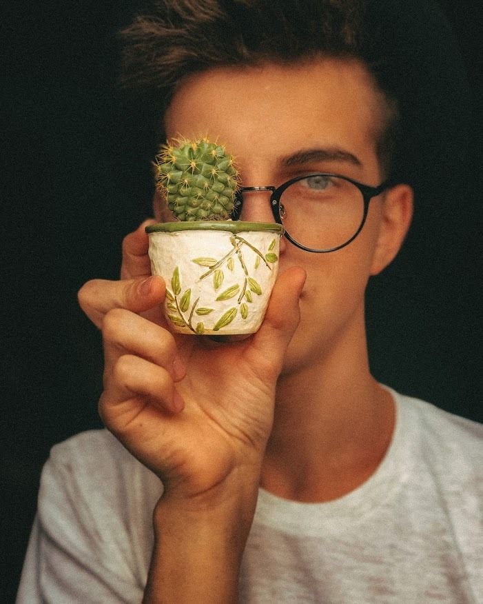 a man holding a small potted plant in front of his face while wearing glasses