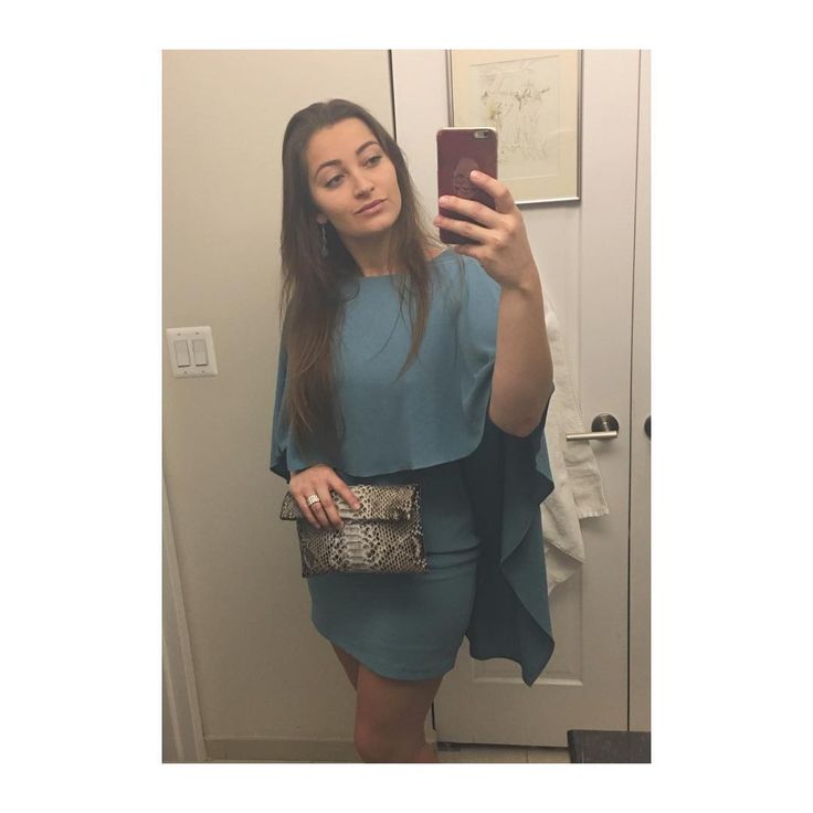 a woman taking a selfie with her cell phone in front of a mirror wearing a blue dress