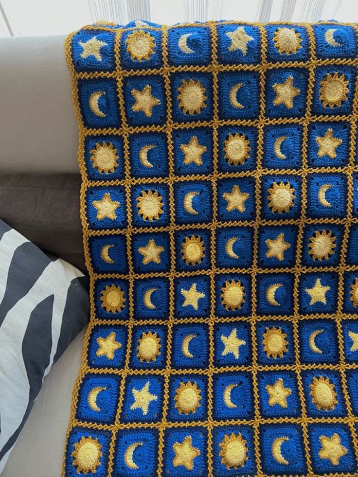 a crocheted blanket with stars and crescents on it, sitting next to a pillow