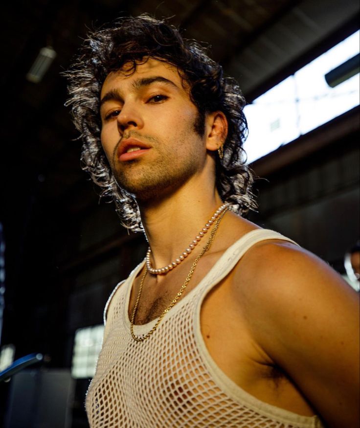 a man with curly hair wearing a white tank top and silver chain necklace on his neck