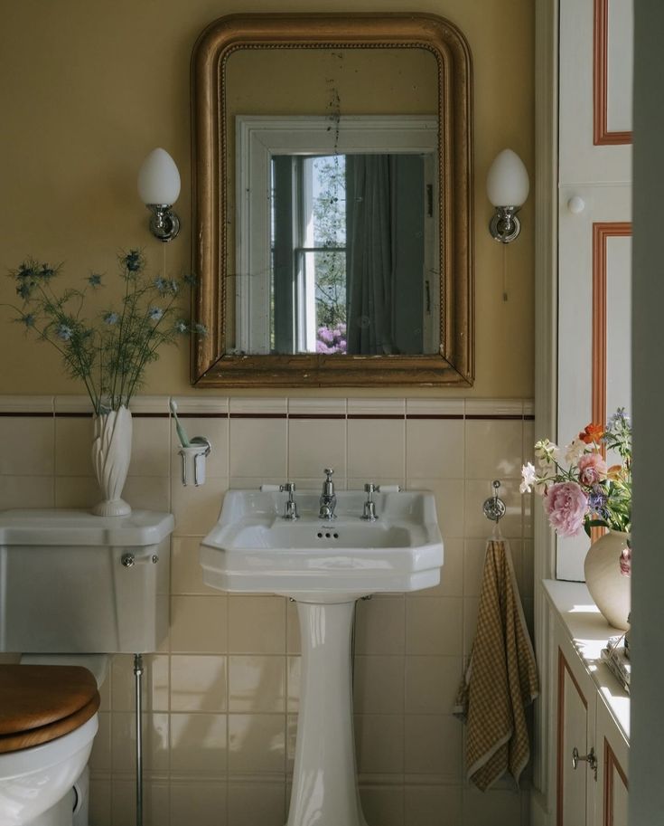 a white pedestal sink sitting under a mirror in a bathroom next to a wooden toilet