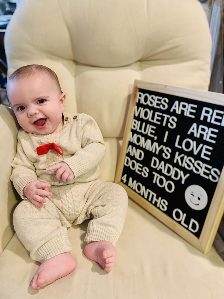 a baby sitting in a chair next to a sign that says roses are red violets are blue i love mom's kisses and dad does too 4 months old