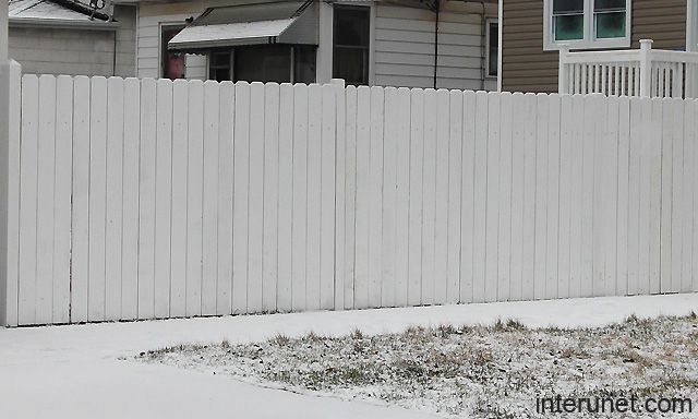 a white picket fence in front of a house with snow on the ground and grass