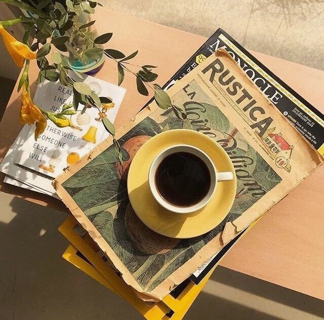 a cup of coffee sitting on top of a table next to a newspaper and vase with flowers