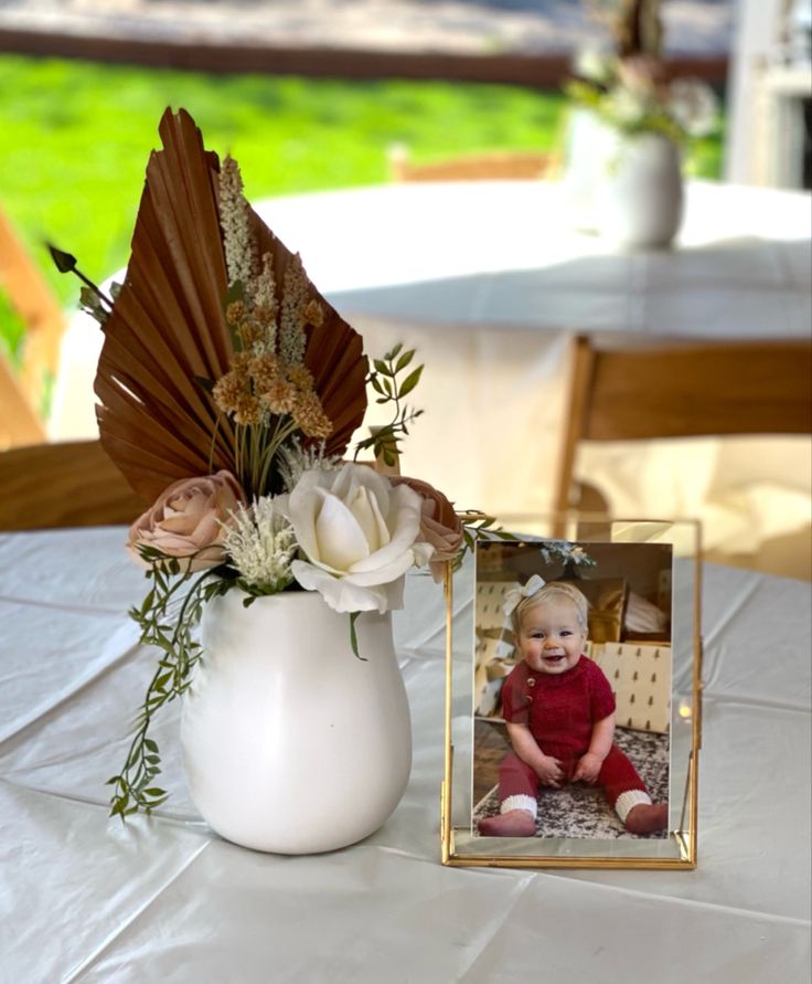 there is a vase with flowers in it next to a picture frame on the table