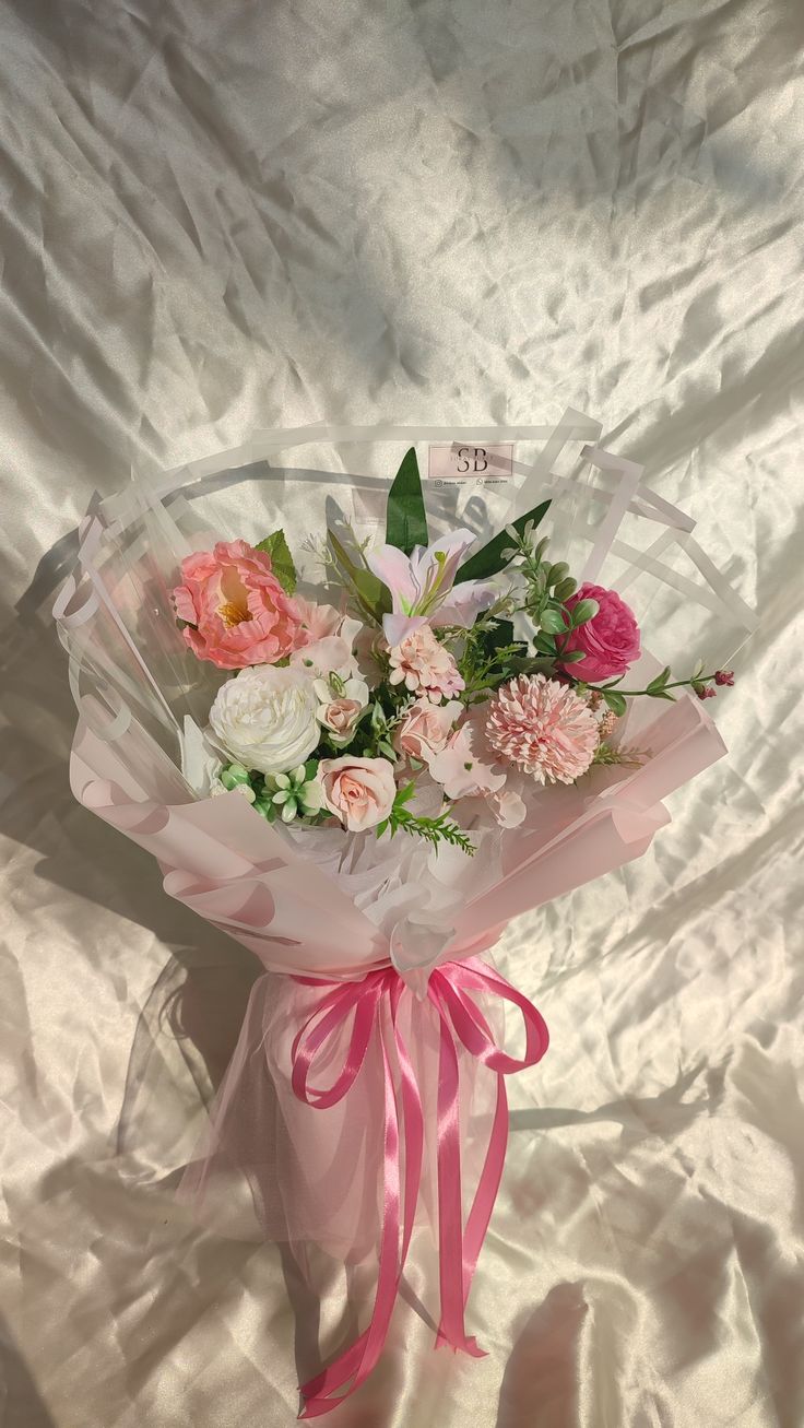 a bouquet of flowers wrapped in pink ribbon on a white sheeted surface with shadows