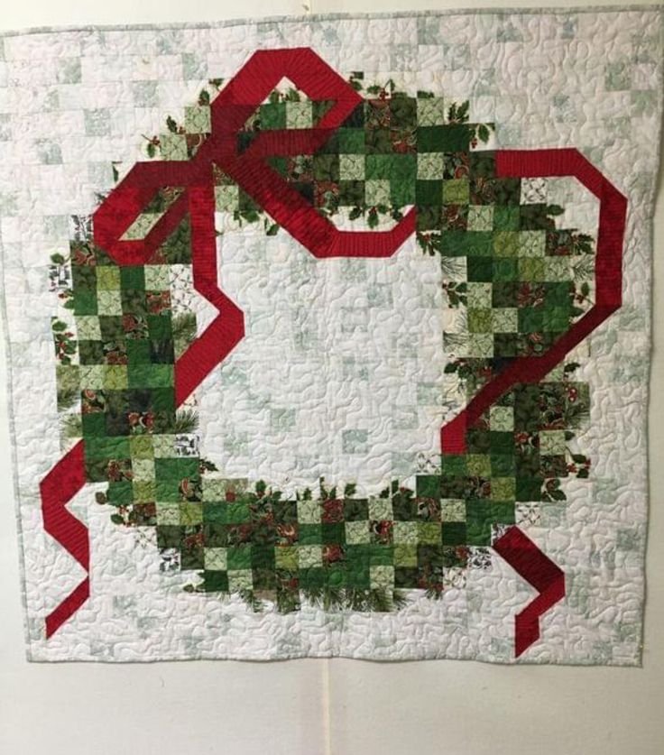 a quilted christmas wreath with red ribbon hanging on the wall in front of a white wall