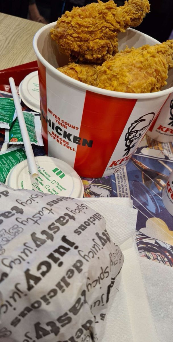 fried chicken in a bucket and paper napkins on a table with other food items