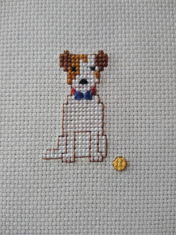 a cross stitch picture of a dog with a blue collar and bow tie sitting next to a yellow ball