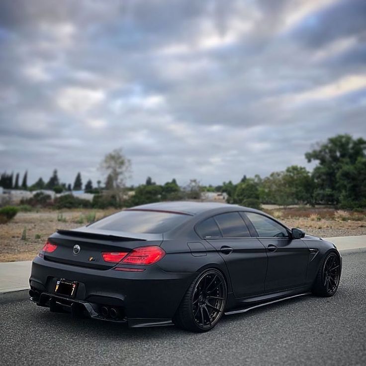 the black car is parked on the side of the road with cloudy skies in the background