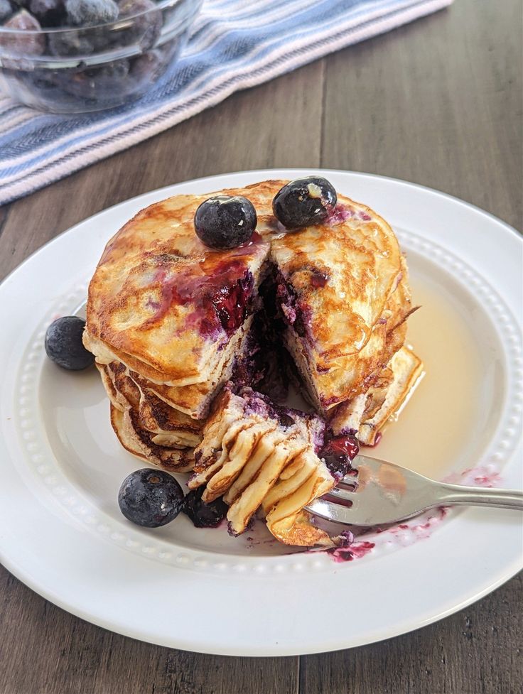 a pancake with blueberries and syrup is on a plate next to a fork