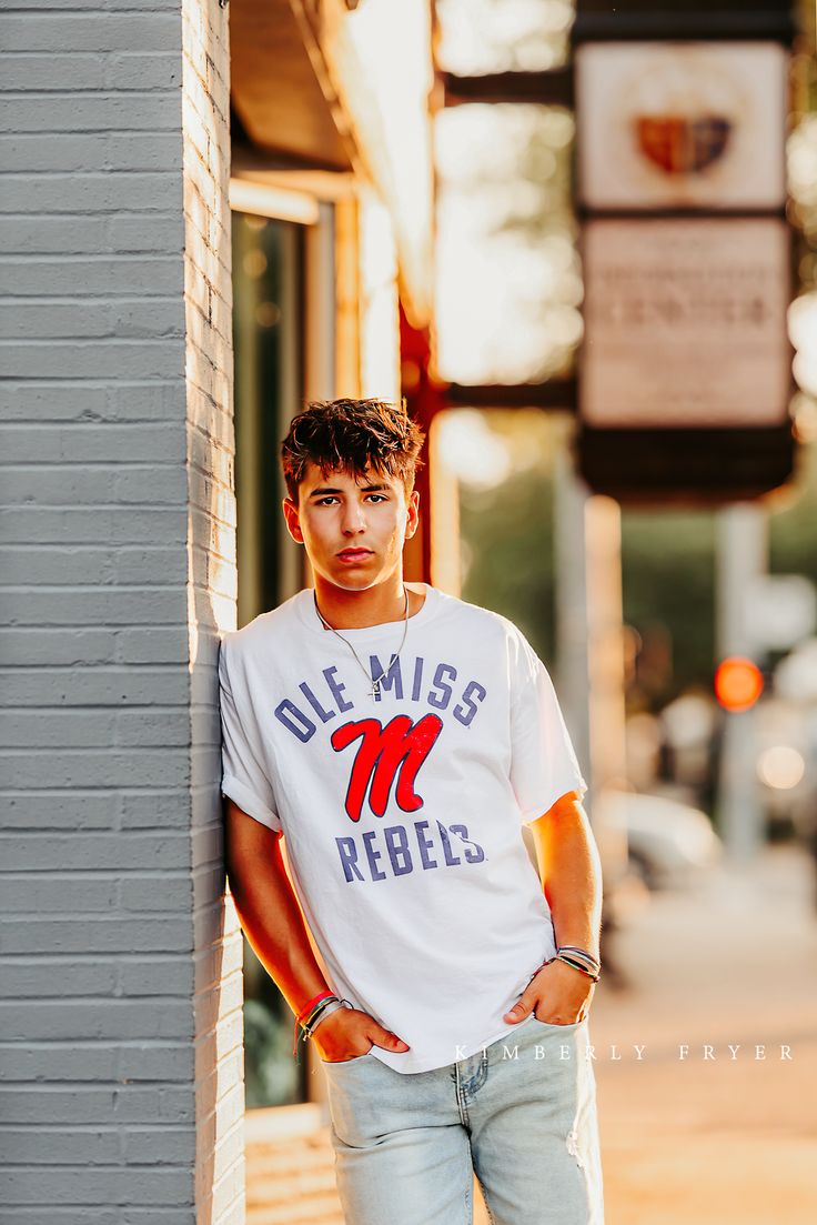 a young man leaning against the side of a building wearing a t - shirt that says ole miss rebel