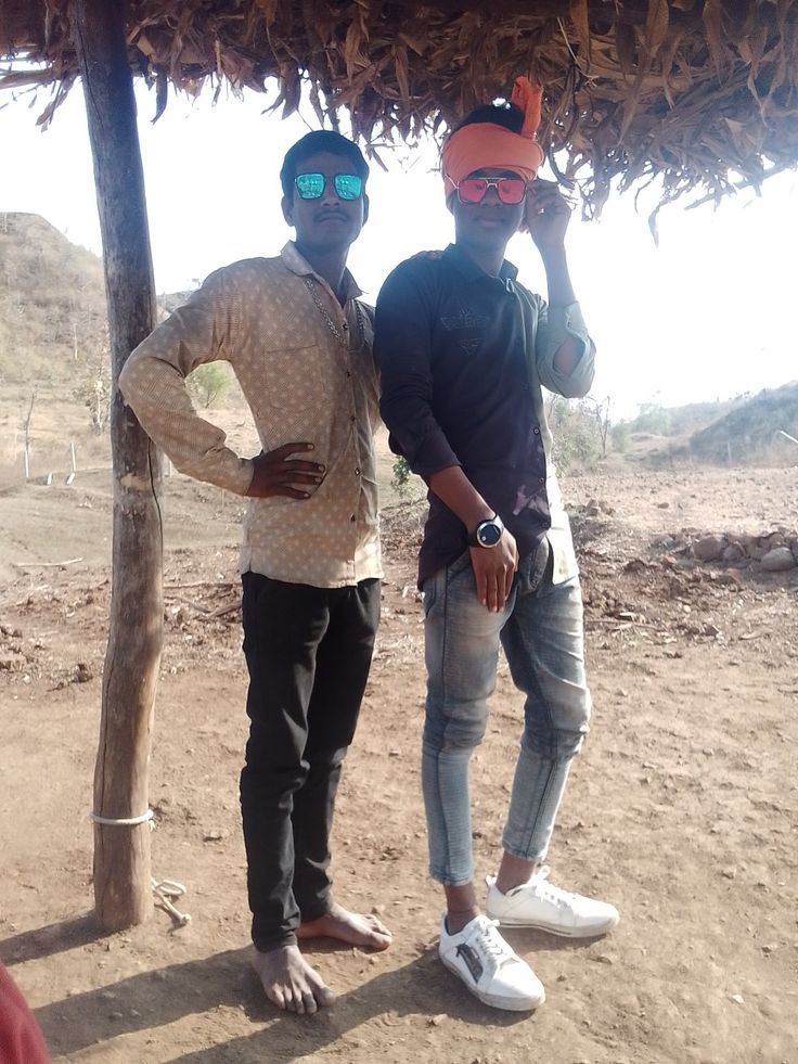 two men standing under a thatched roof with their hands on their hipss and wearing sunglasses