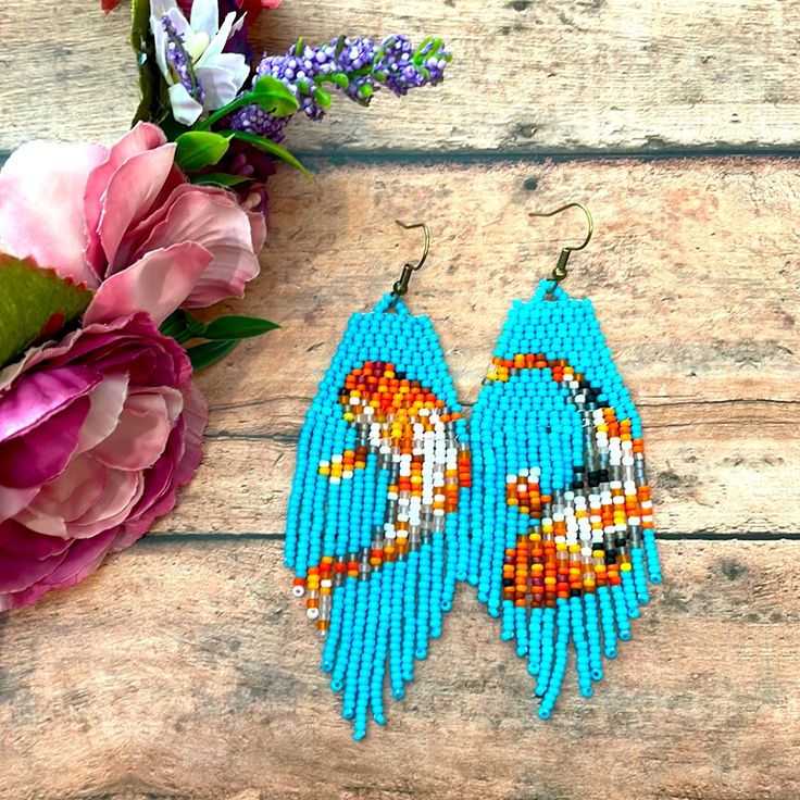 a pair of blue beaded earrings sitting on top of a wooden table next to flowers