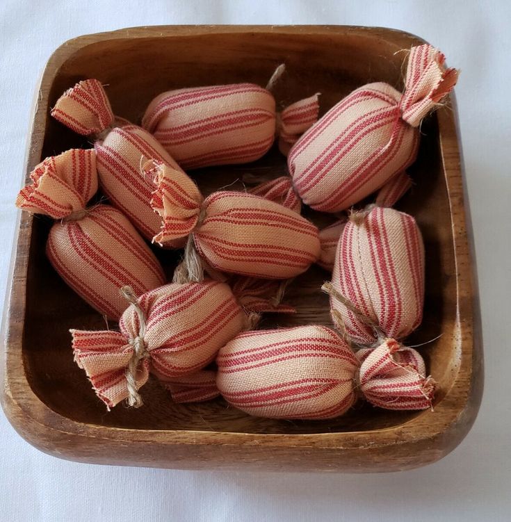 a wooden bowl filled with red and white striped fabric balls on top of a table