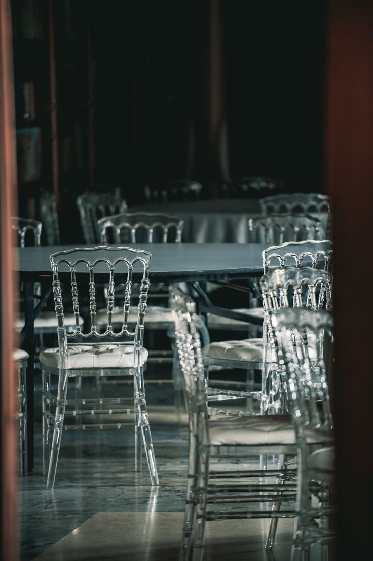 chairs and tables are lined up in a room with dark lighting from the window behind them