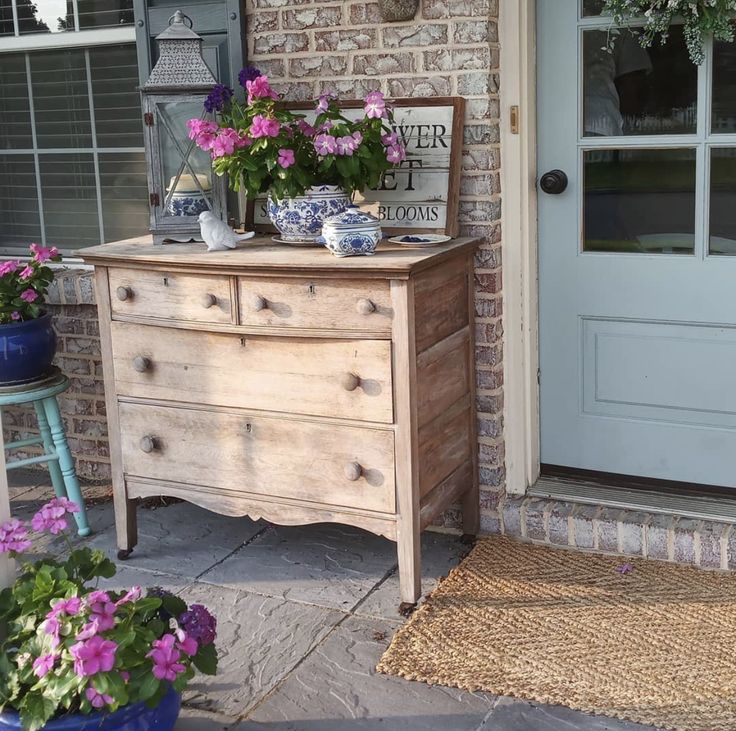 an old dresser with flowers on it sitting in front of a brick wall and door