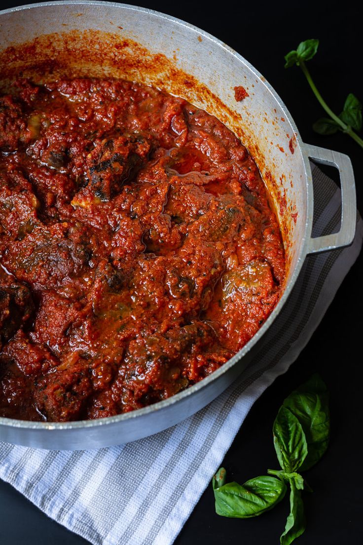 a large pot filled with meat and sauce on top of a towel next to basil leaves