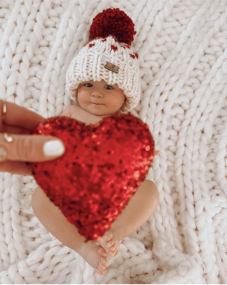 a baby wearing a santa hat and holding a red heart shaped pillow in it's hand