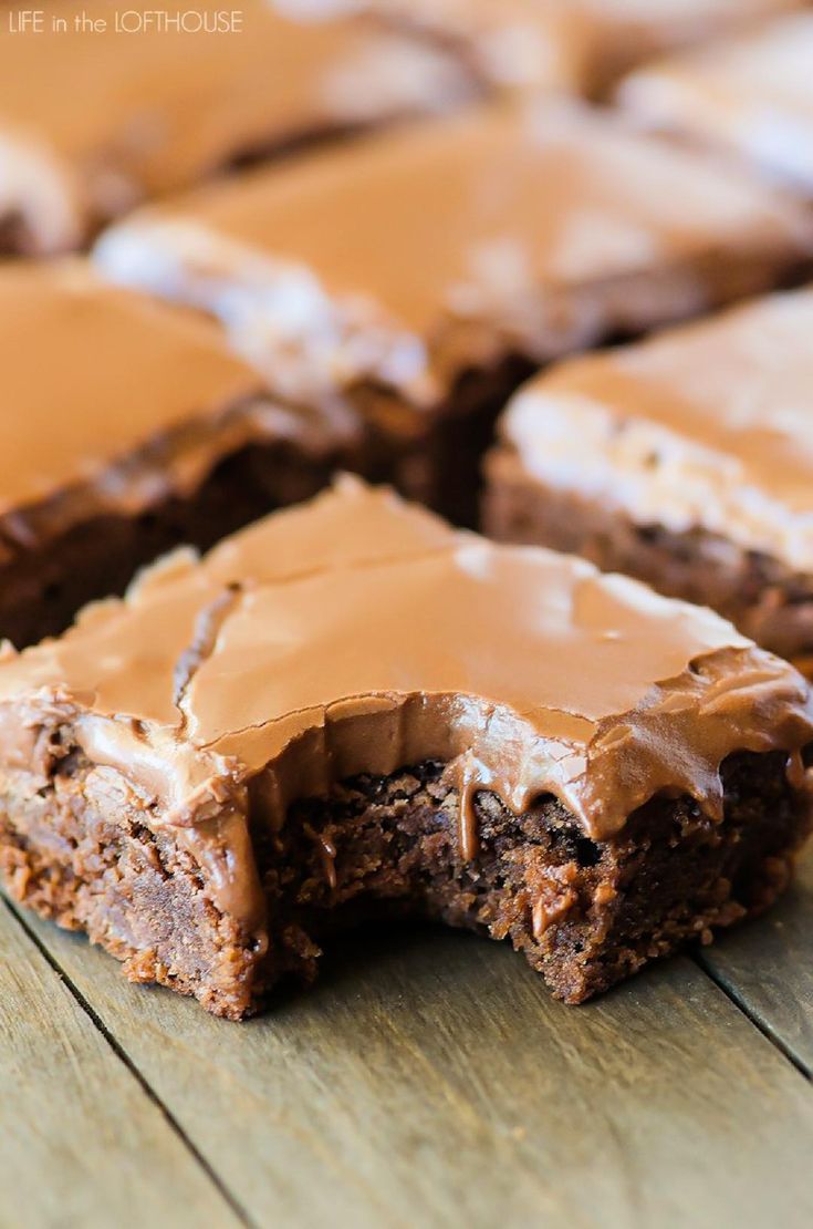 chocolate brownies with peanut butter frosting cut in half on a wooden table, ready to be eaten