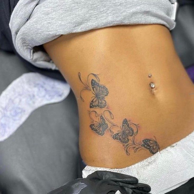 a woman's stomach with butterfly tattoos on her lower back and the bottom part of her abdomen