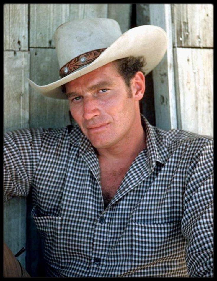 a man wearing a cowboy hat leaning against a wooden wall