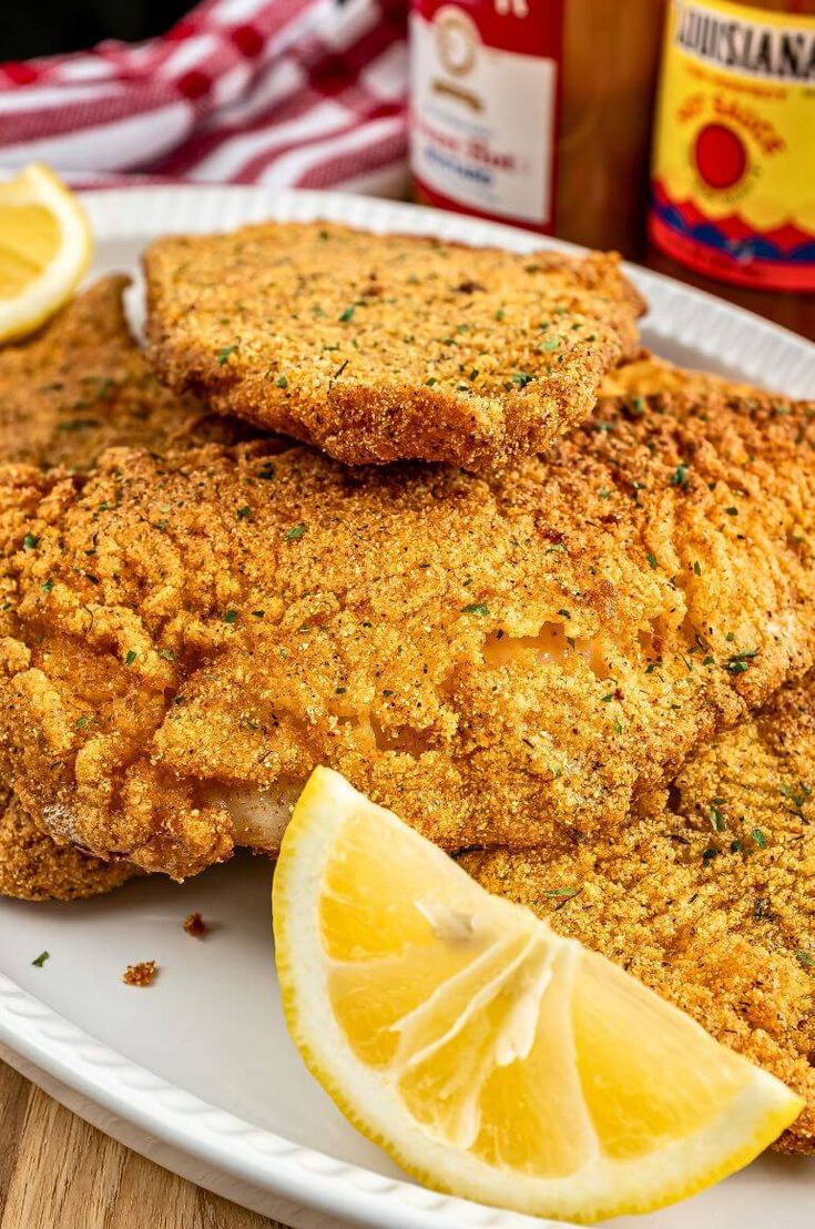 two pieces of fried fish on a plate with lemon wedges