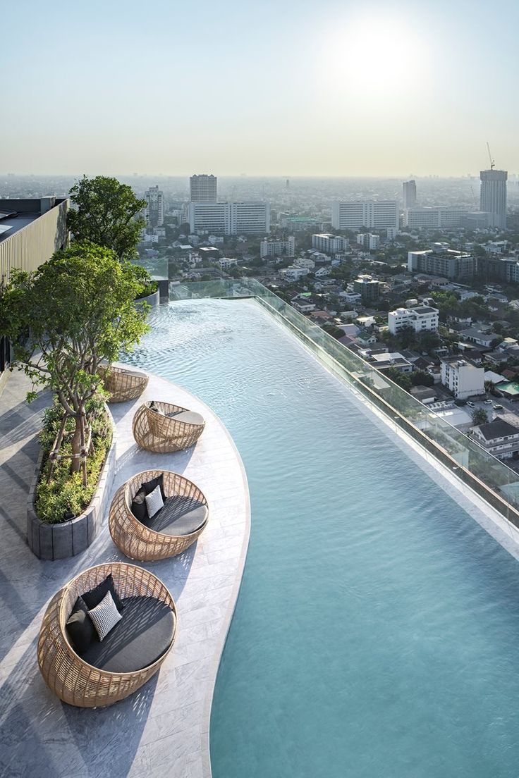 an outdoor swimming pool with lounge chairs and trees on the edge, overlooking a cityscape