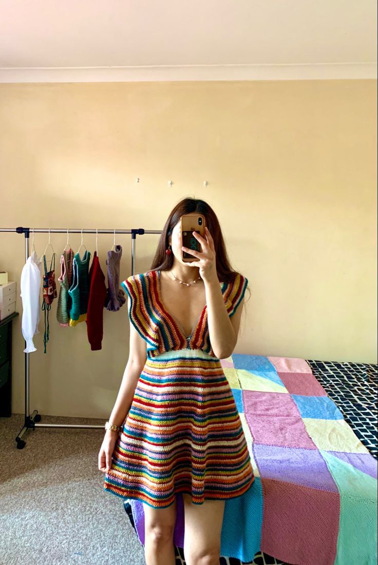 a woman taking a selfie in front of a bed with clothes hanging on the rack