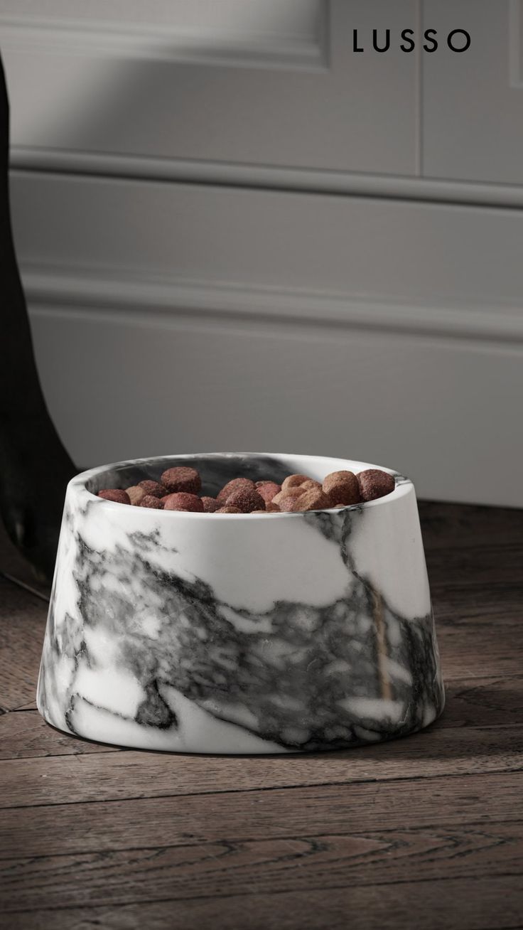 a marble bowl with nuts in it sitting on a wooden floor next to a black and white wall