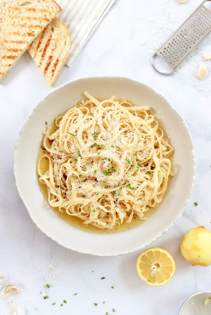 a white bowl filled with pasta and topped with parmesan cheese next to sliced lemons