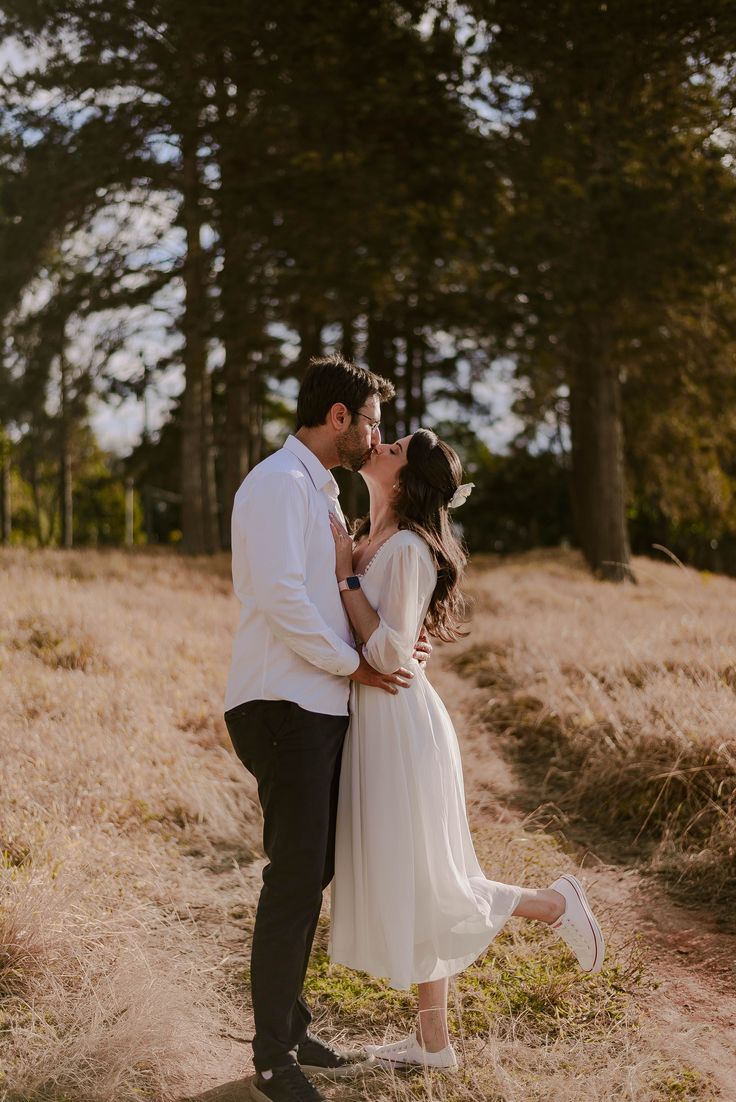 a man and woman kissing in the middle of a field with tall grass on both sides