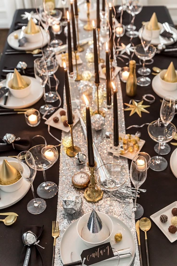 a long table is set with silver and gold place settings, candles, and plates