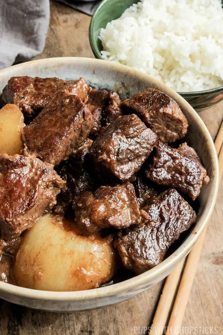 a bowl filled with beef and potatoes next to rice