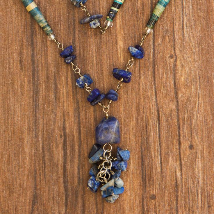 Sodalite's rich shades of blue find a complement in handcrafted beads. Francis Oliveira recycles magazines to adorn a delightful necklace. Linked with brass rings the varnished paper cylinders combine with gemstones and culminate in an ornate pendant. The necklace loops around the neck as desired. Artisan Blue Necklace, Handmade Bohemian Kyanite Jewelry, Bohemian Sapphire Necklaces With Natural Stones, Handmade Kyanite Healing Necklaces, Handmade Sapphire Kyanite Necklace, Handmade Sapphire Necklace In Kyanite, Handmade Bohemian Sapphire Necklace, Handmade Artisan Lapis Lazuli Necklace, Recycled Magazines