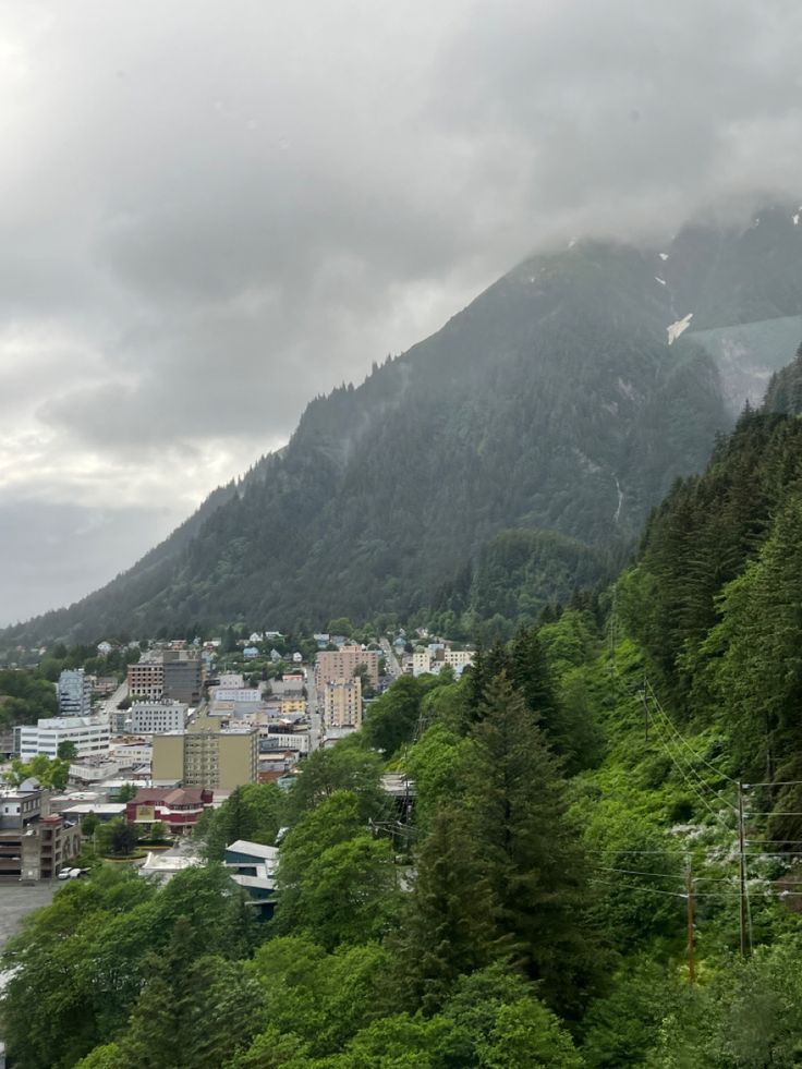 a city with mountains in the background and trees on both sides, under cloudy skies