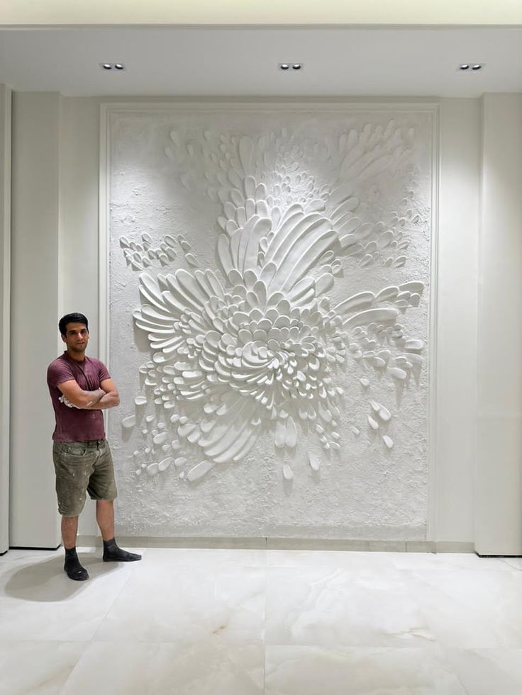 a man standing in front of a white wall with an intricate flower design on it