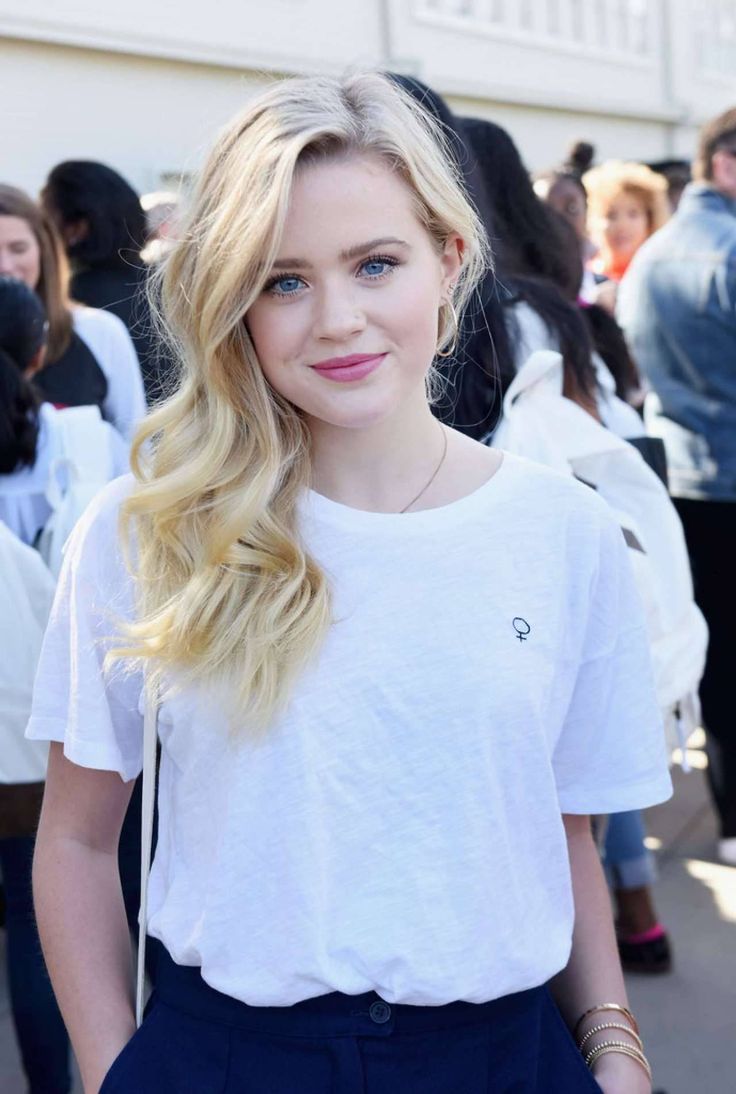 a woman with long blonde hair wearing a white t - shirt and dark blue pants