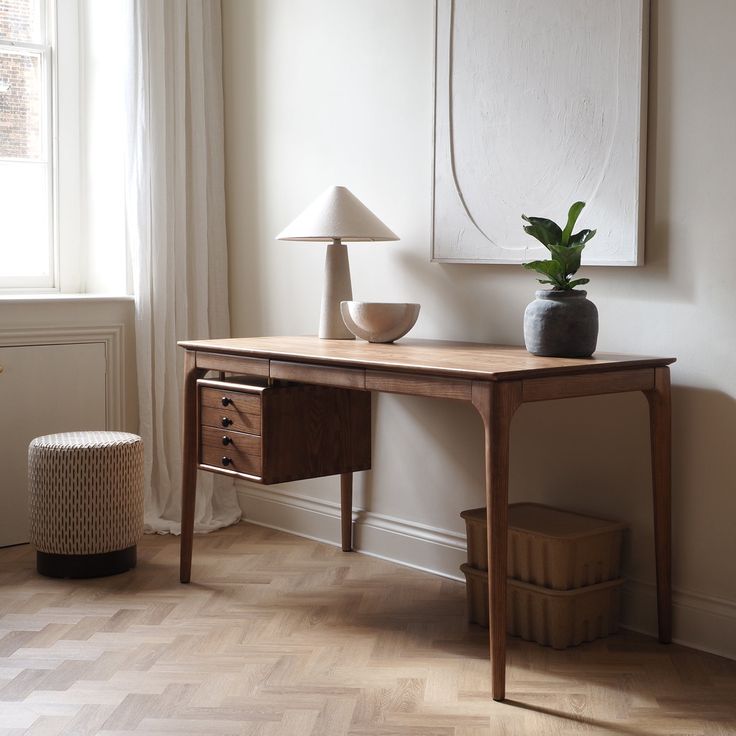 a wooden table with a lamp on top of it next to a painting and a basket