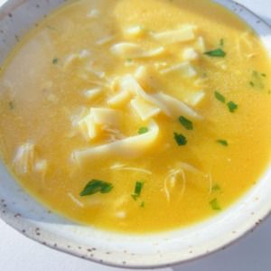 a bowl of soup with cheese and parsley in it on a white tablecloth