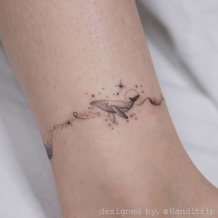 a small tattoo on the ankle of a woman's foot with a whale and stars