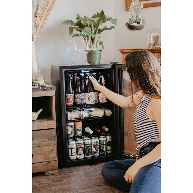 a woman sitting on the floor in front of an open refrigerator filled with beer bottles