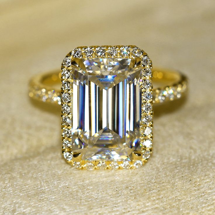 Classic Selina 5.5ct Elongated Emerald-cut Moissanite and Lab Diamond Halo Engagement ring in 14K or 18K Gold. The Selina engagement ring features a 5.5ct elongated emerald-cut moissanite center stone surrounded by a halo of lab-grown diamonds in a slim basket setting. The shank is illuminated with pavé lab-grown diamonds in a semi-eternity fashion. Like a classic romance with a modern flare, our very popular Selina collection was born from our affinity to stories rooted in the beauty of love an Emerald Cut Halo Ring, Engagement Rings 4 Carat, Emerald Cut Halo, Classic Romance, Basket Setting, Emerald Cut Moissanite, Diamond Halo Engagement Ring, Classic Engagement Rings, Band Engagement Ring