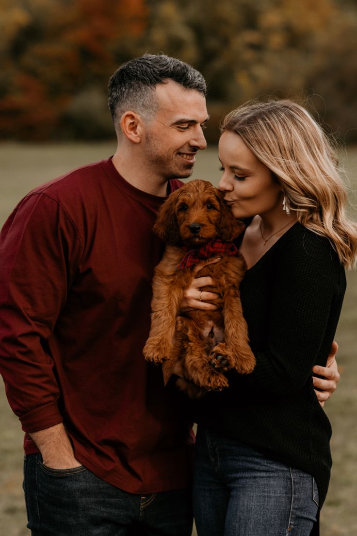 a man and woman standing next to each other holding a brown dog in their arms