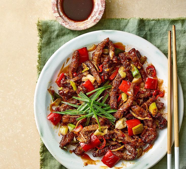 a white plate topped with meat and vegetables next to chopsticks